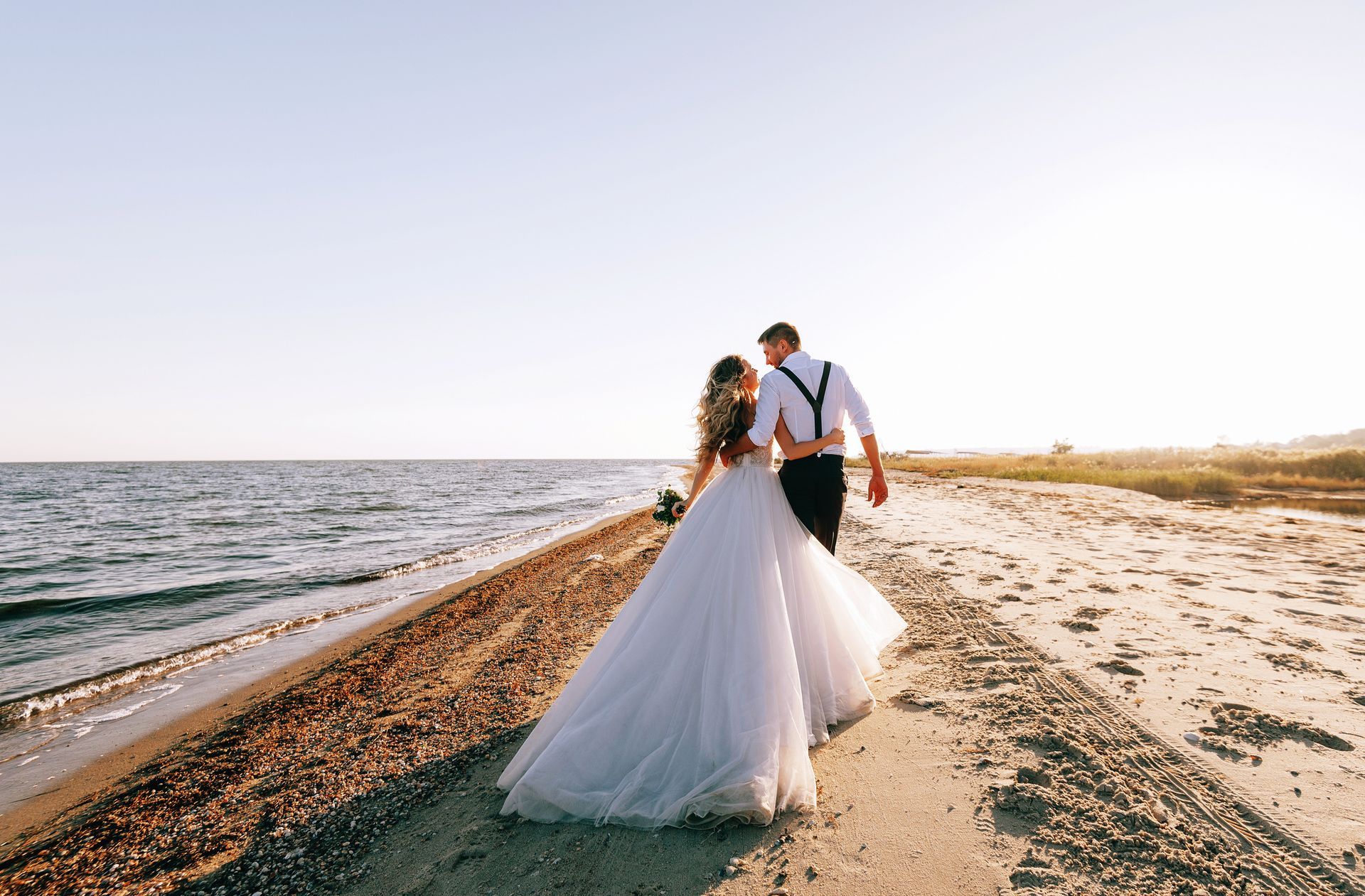 Bride and groom walking hand in hand along a beach at sunset