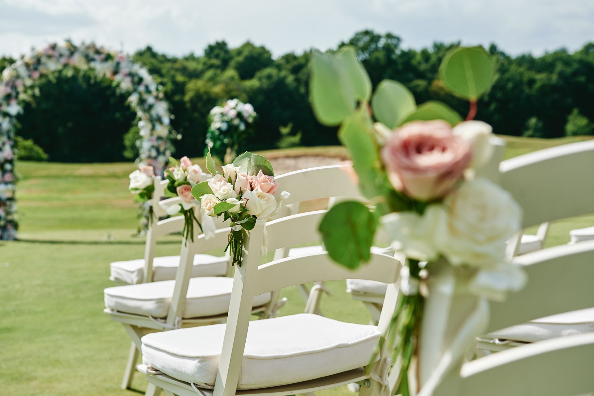 White chairs with pastel flower arrangements on a sunny outdoor wedding lawn
