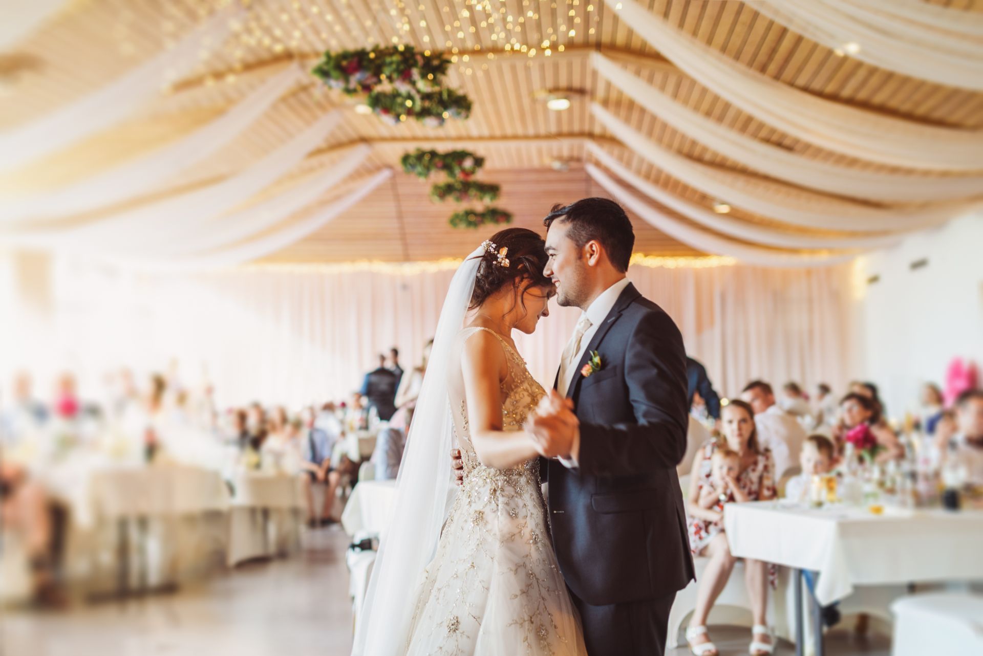 Bride and groom slow dancing at a bright wedding reception under draped ceiling decor