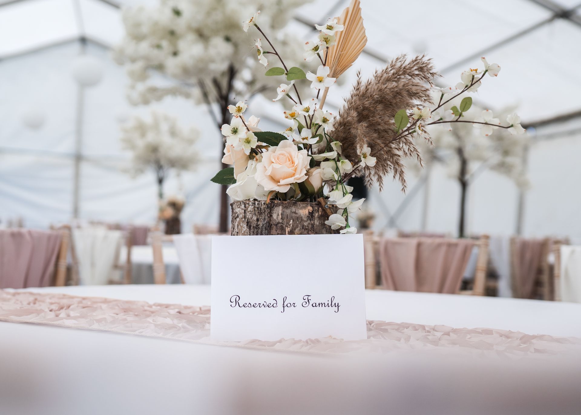 Floral wedding centerpiece with cream flowers and pampas grass on a white reception table outdoors