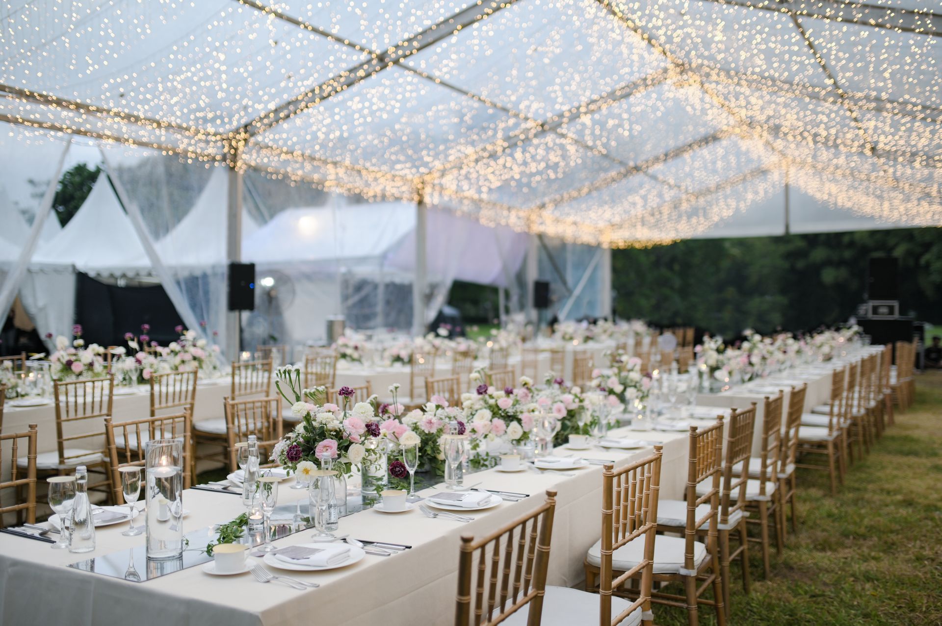 Elegant outdoor wedding reception setup under twinkling lights with long white-clothed tables and floral centerpieces