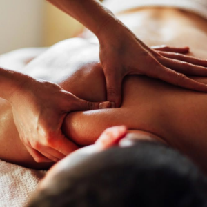 Hands giving a back massage on a person lying face down on a bed