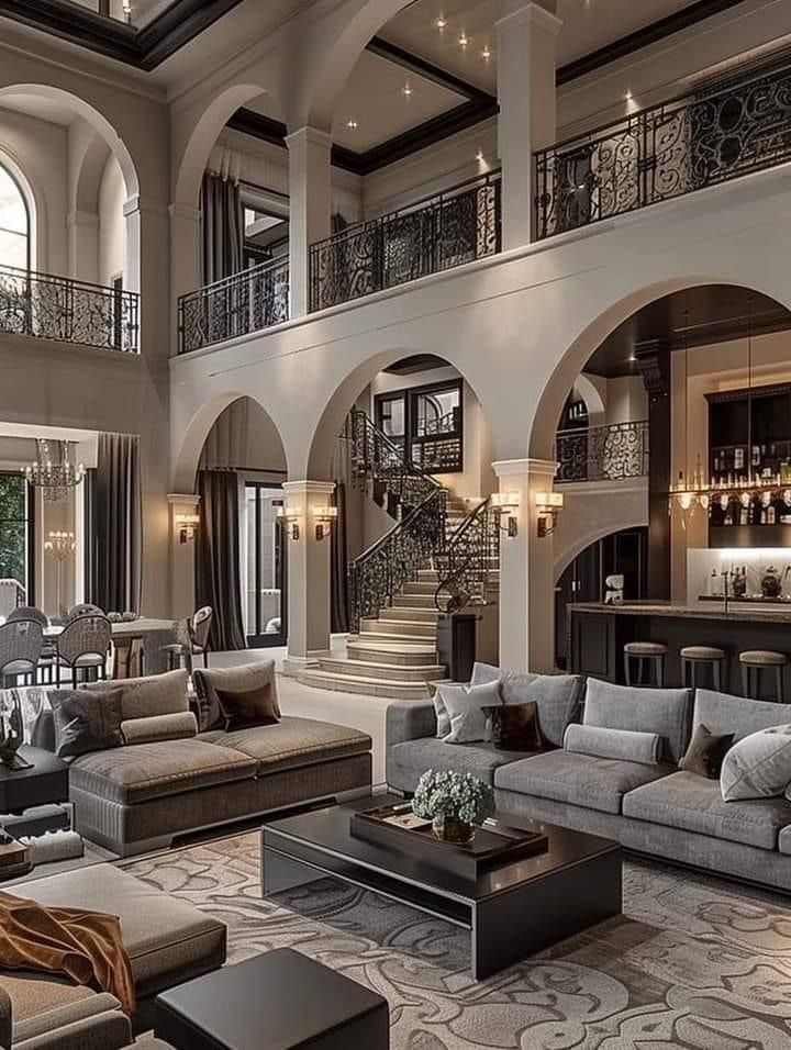 Elegant two-story living room with arches, chandelier, gray sofas, and a grand staircase