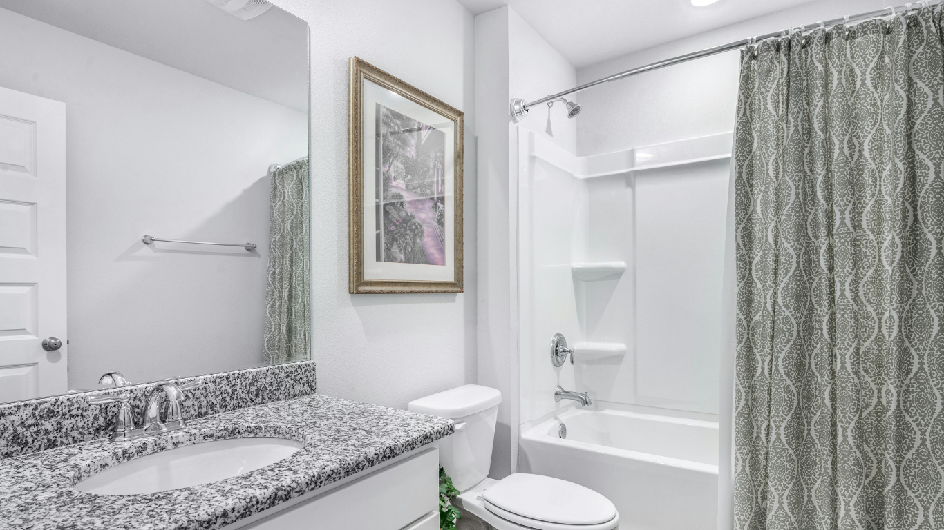 A modern bathroom with a granite vanity, white toilet, and a bathtub with a patterned gray shower curtain.