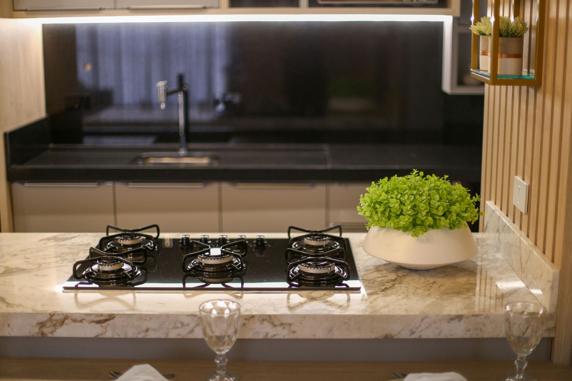 A modern kitchen featuring a black glass stovetop on a marble countertop, with a potted plant and sink in the background.