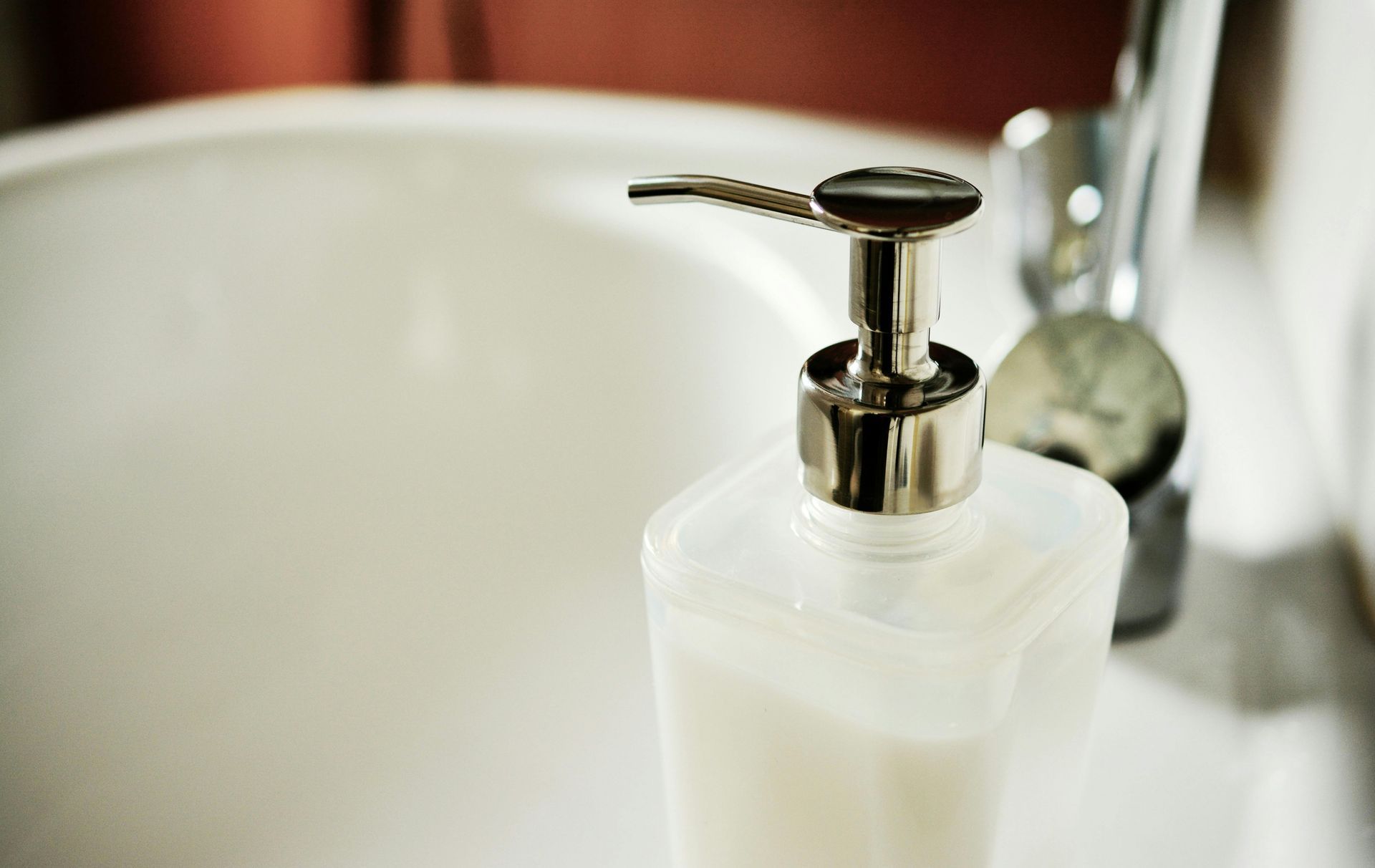 A translucent square soap dispenser with a silver pump sits on the edge of a white bathroom sink.