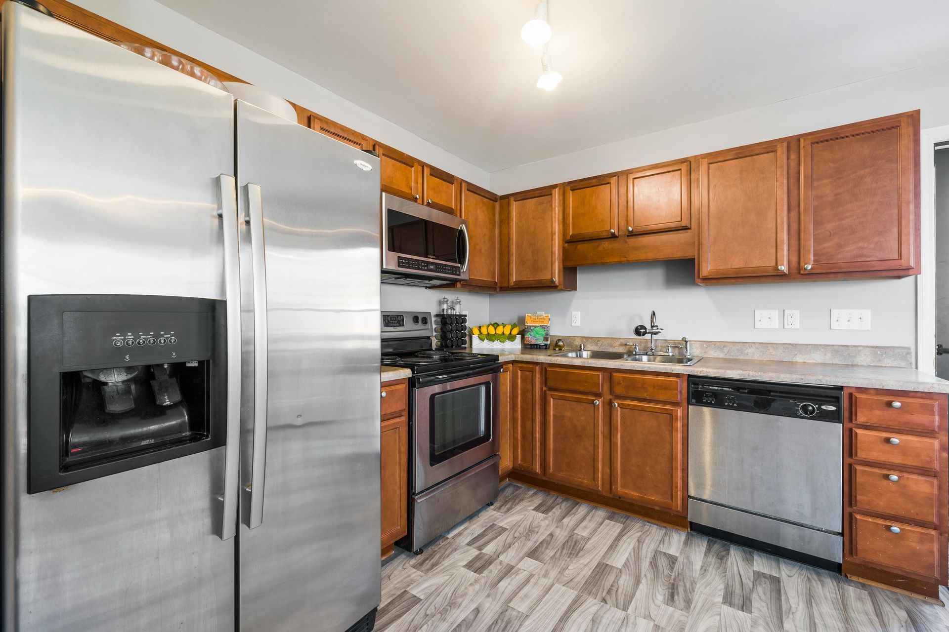 A modern kitchen with brown cabinets, stainless steel appliances, a grey patterned floor, and light grey walls.