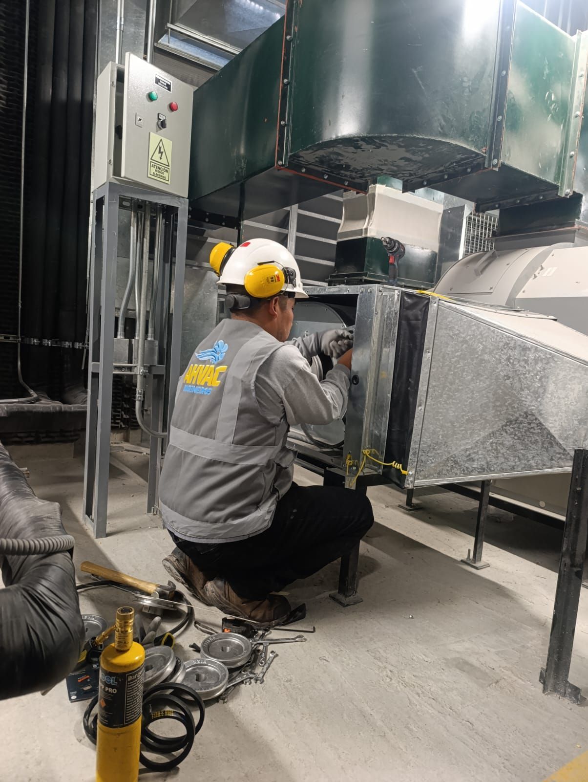 Un trabajador se arrodilla junto a un gran conducto de ventilación