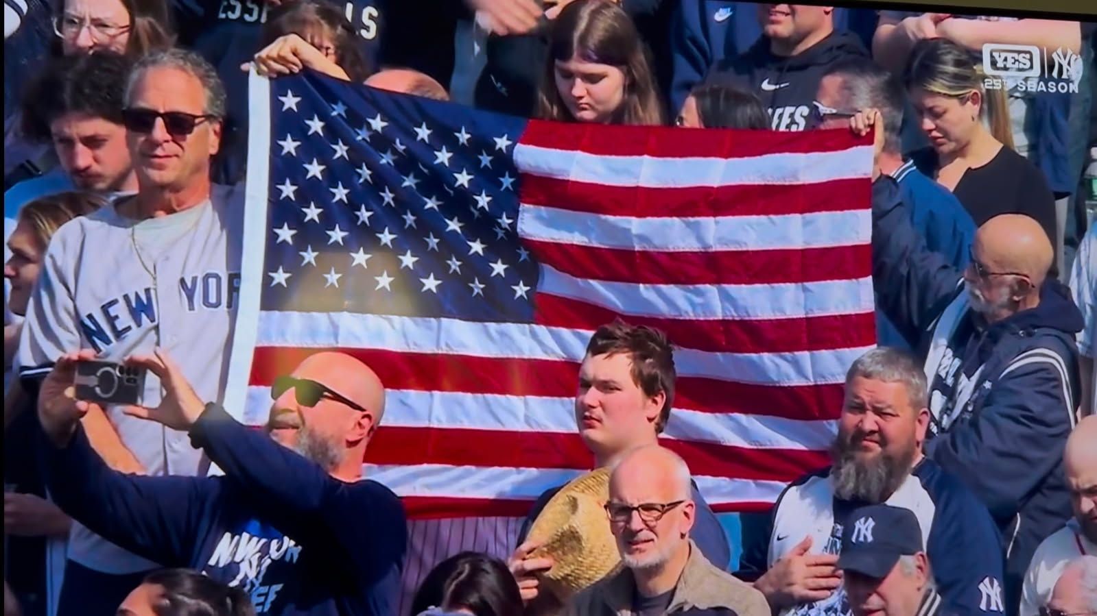 Crowd at a sports event holding and waving a large American flag