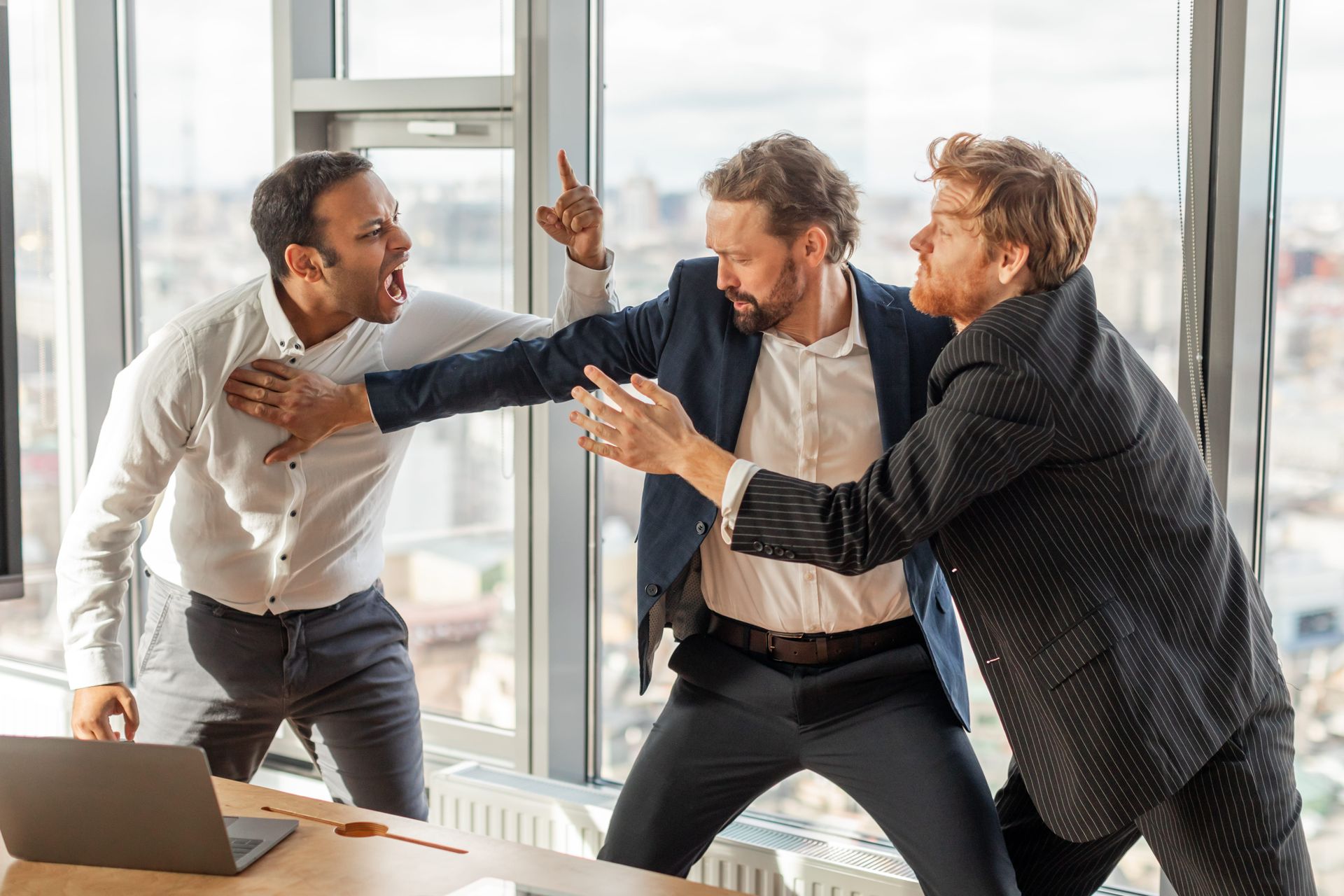 Three office workers arguing beside a laptop in a bright conference room