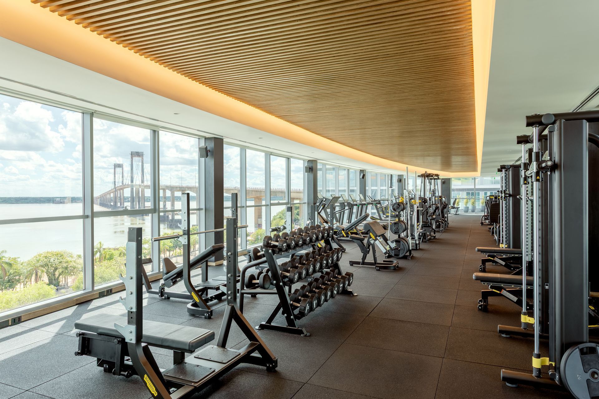 Interior de gimnasio con máquinas de pesas, barras y pesas sobre suelo negro.