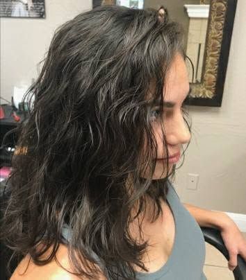 Profile view of a person with wavy dark hair in a gray top, seated indoors against a wall with framed art.