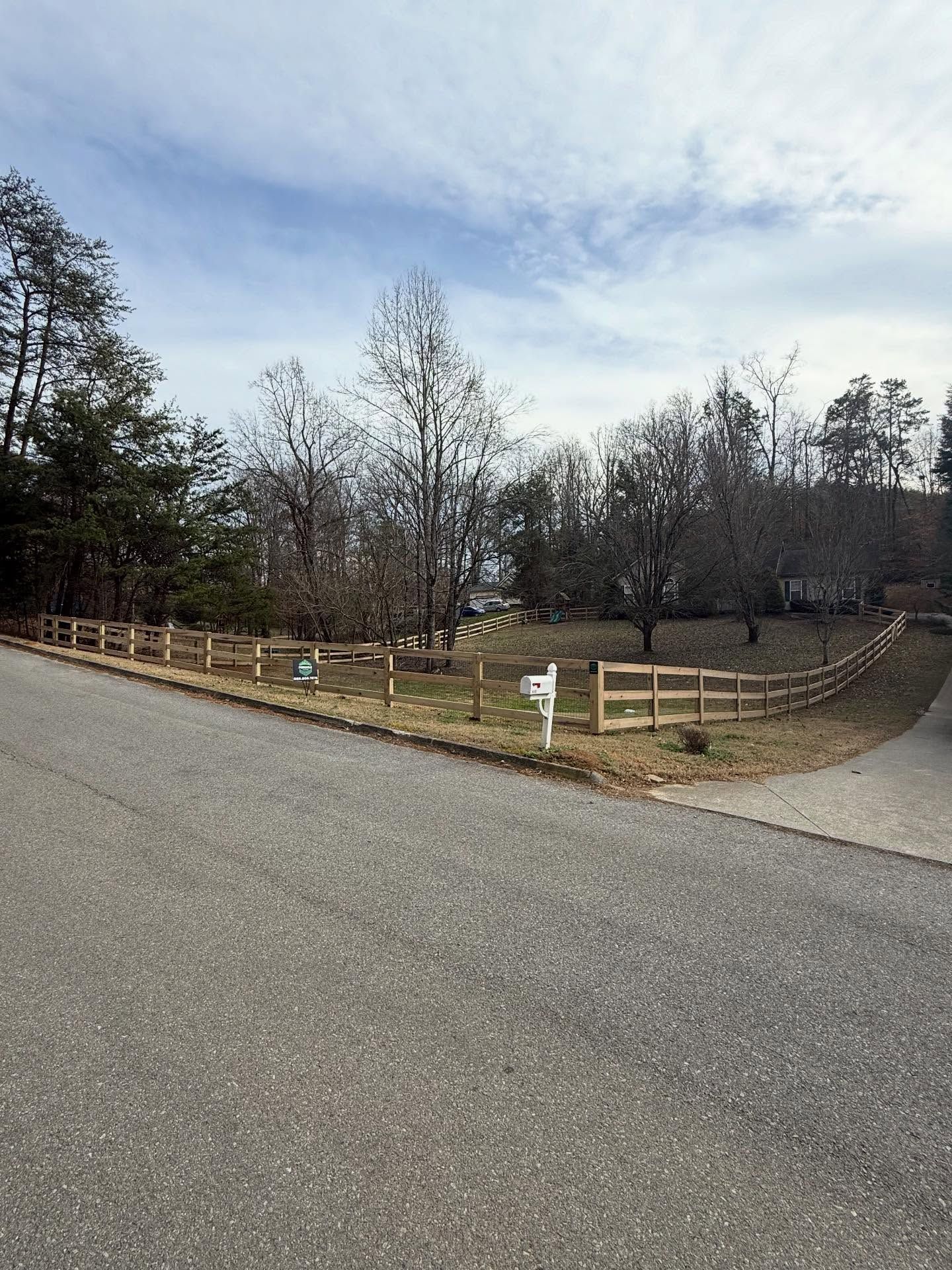 Curved gravel driveway with wooden fencing and bare trees under a cloudy sky