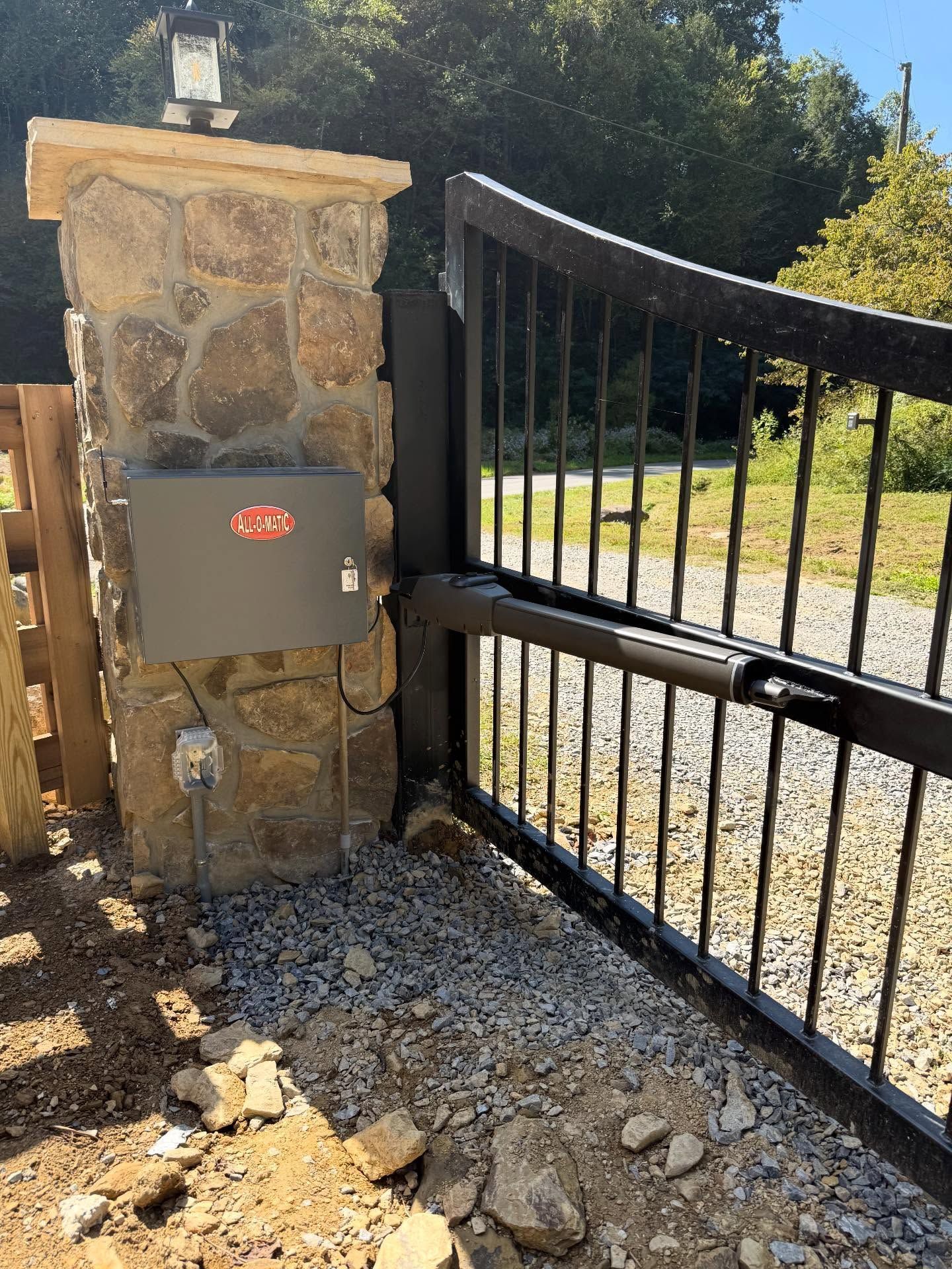 Stone gate pillar with a black metal driveway gate and mailbox controller in sunlight