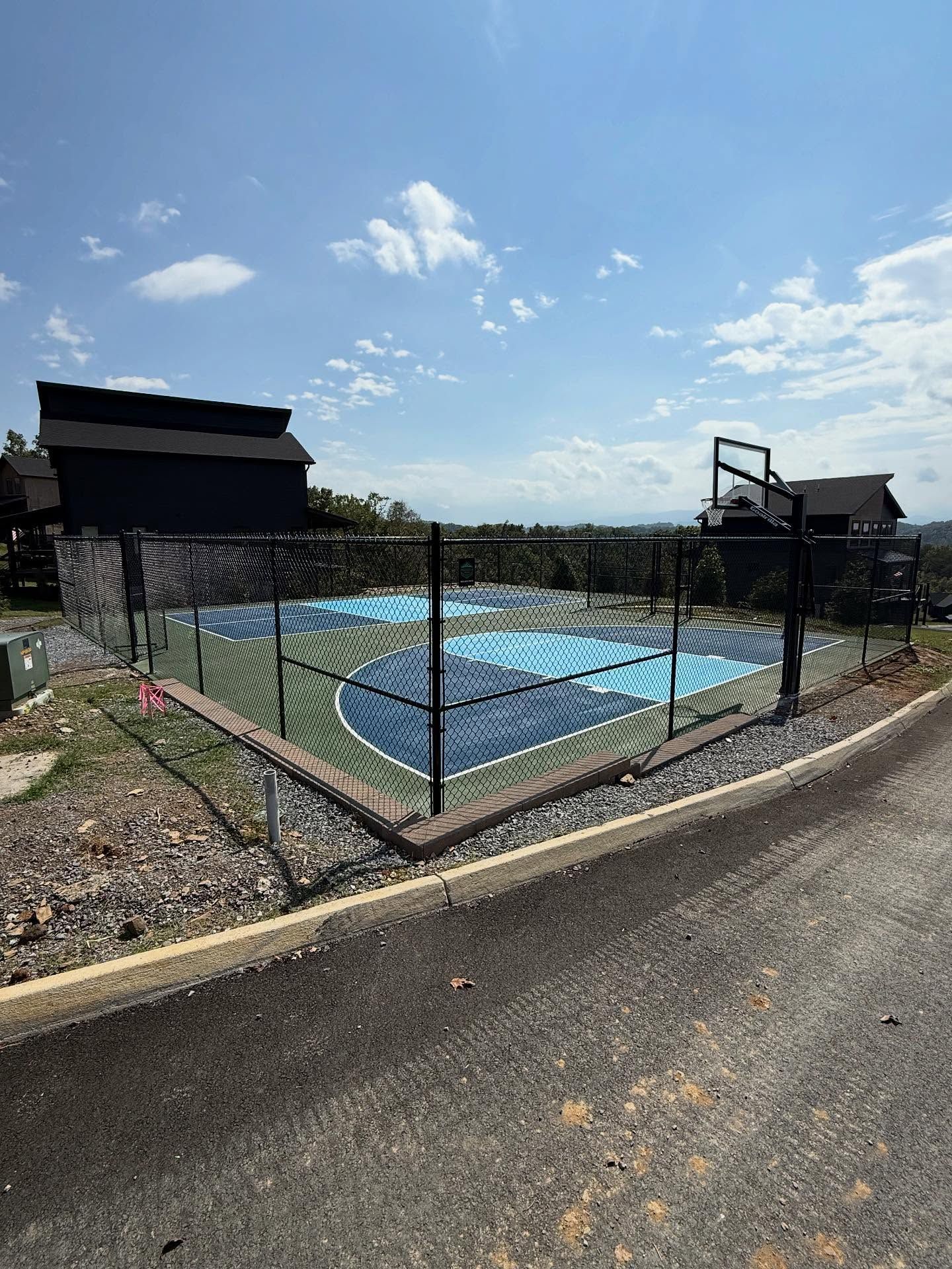 Outdoor fenced basketball court with blue surface and hoop under a sunny sky