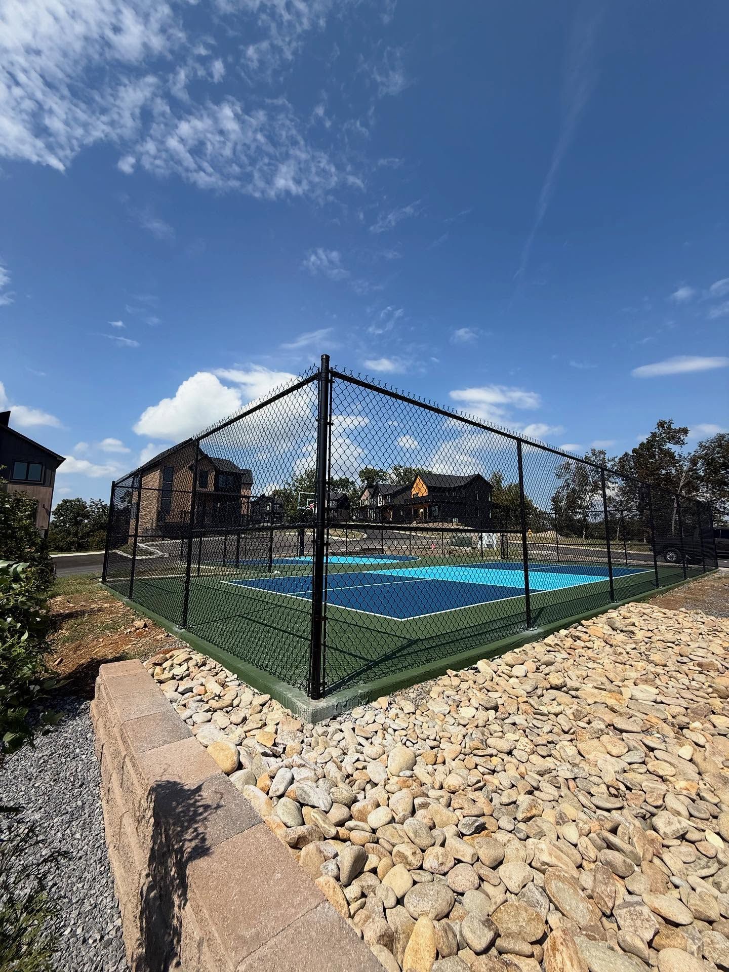 Black chain-link fence around a blue-covered backyard pool beside stone landscaping under a sunny sky