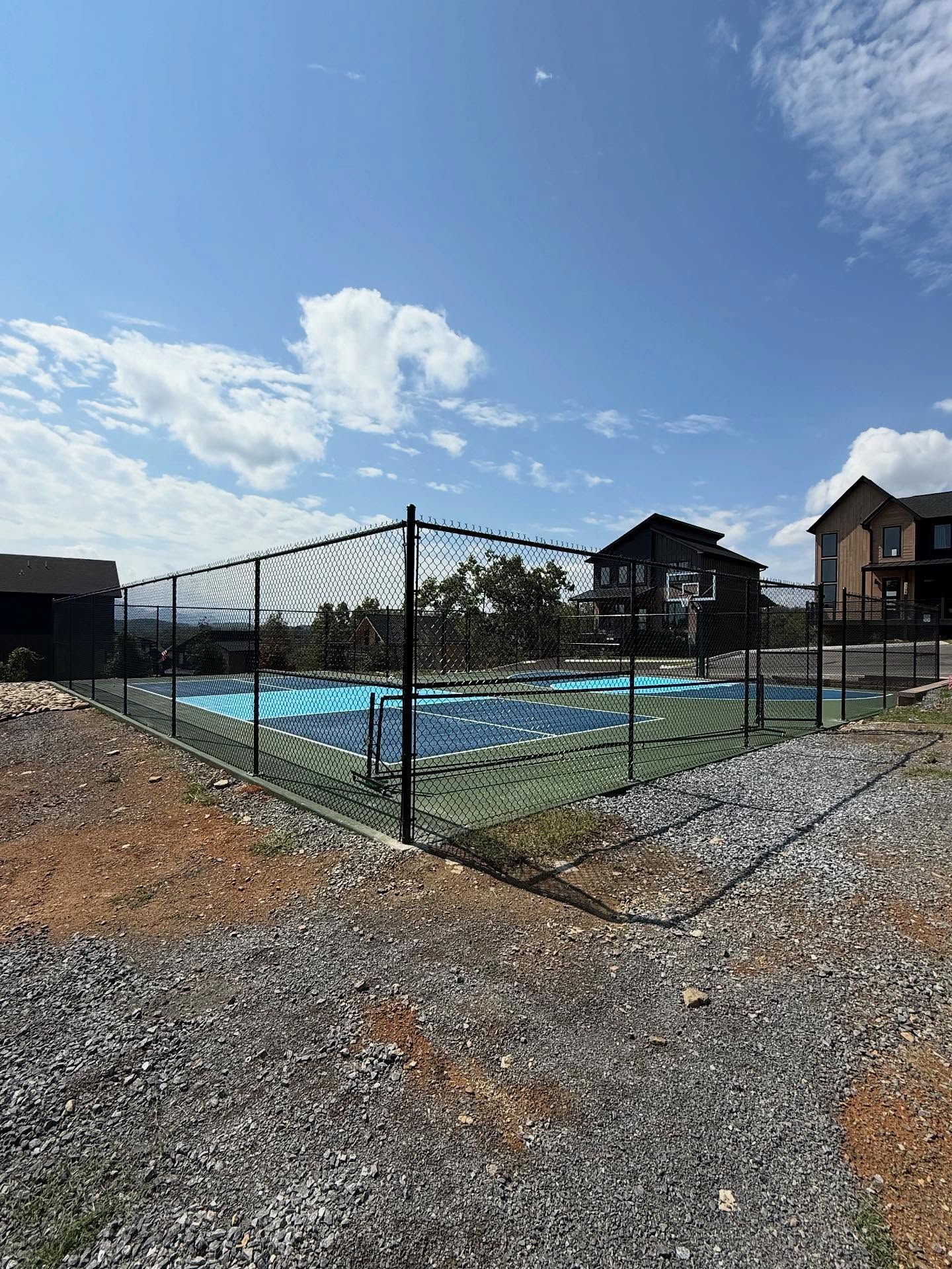 Outdoor swimming pool behind a black chain-link fence under a bright blue sky.