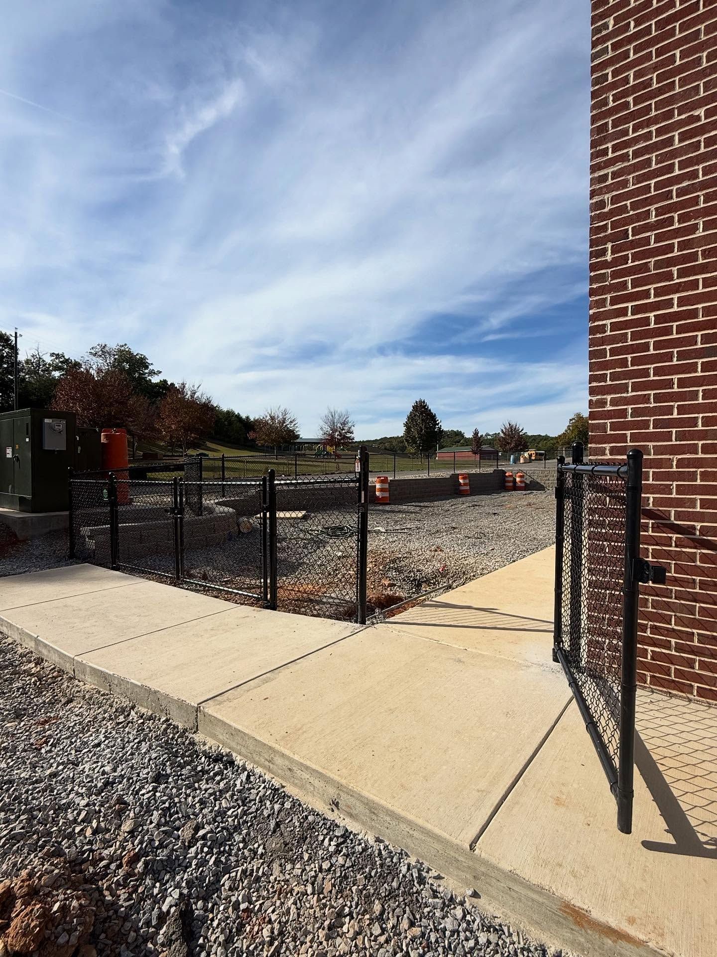 Brick building entrance with open black metal gate leading to a gravel courtyard under a blue sky