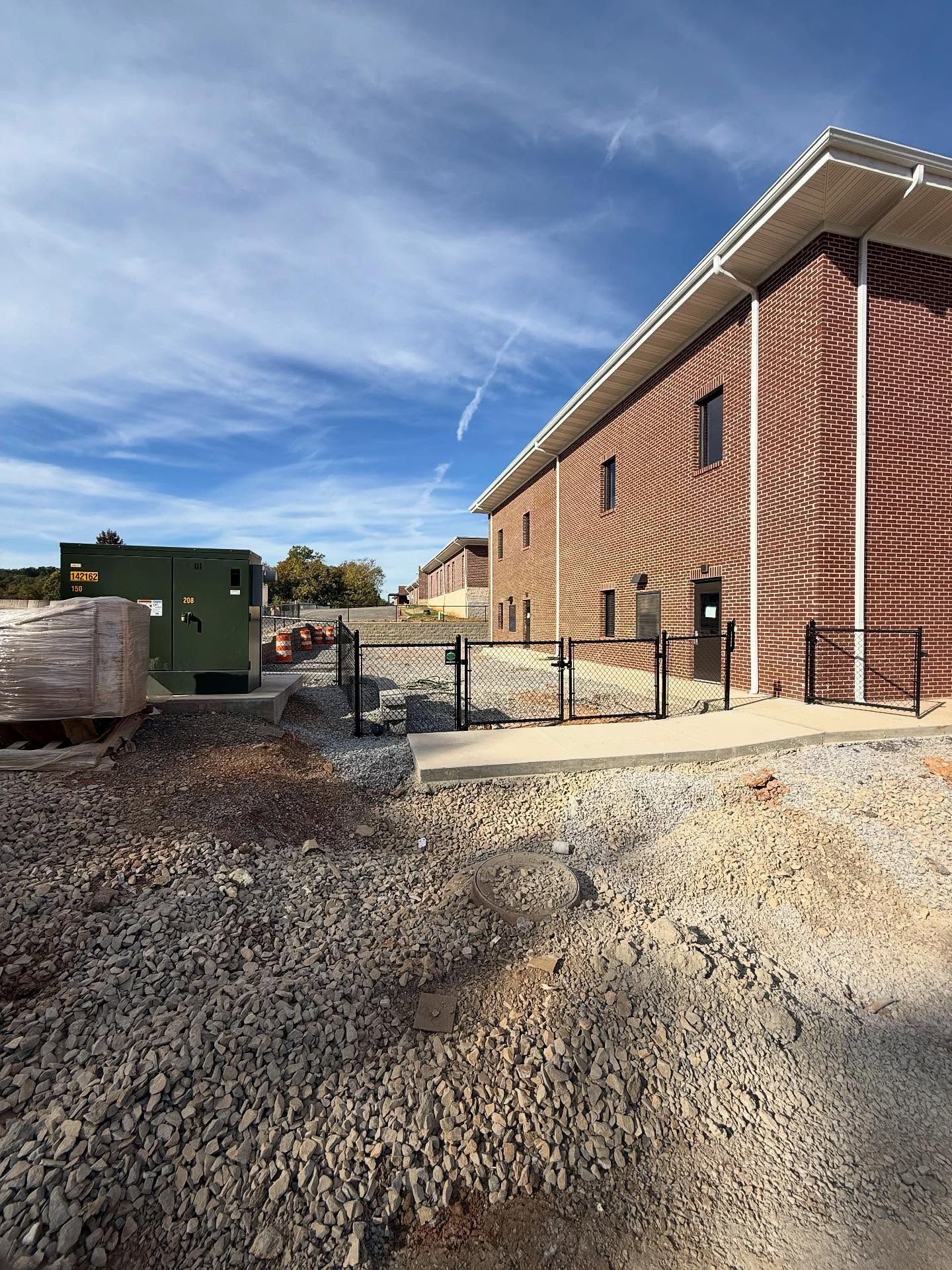 Brick building and gravel lot with a green utility truck under a blue sky