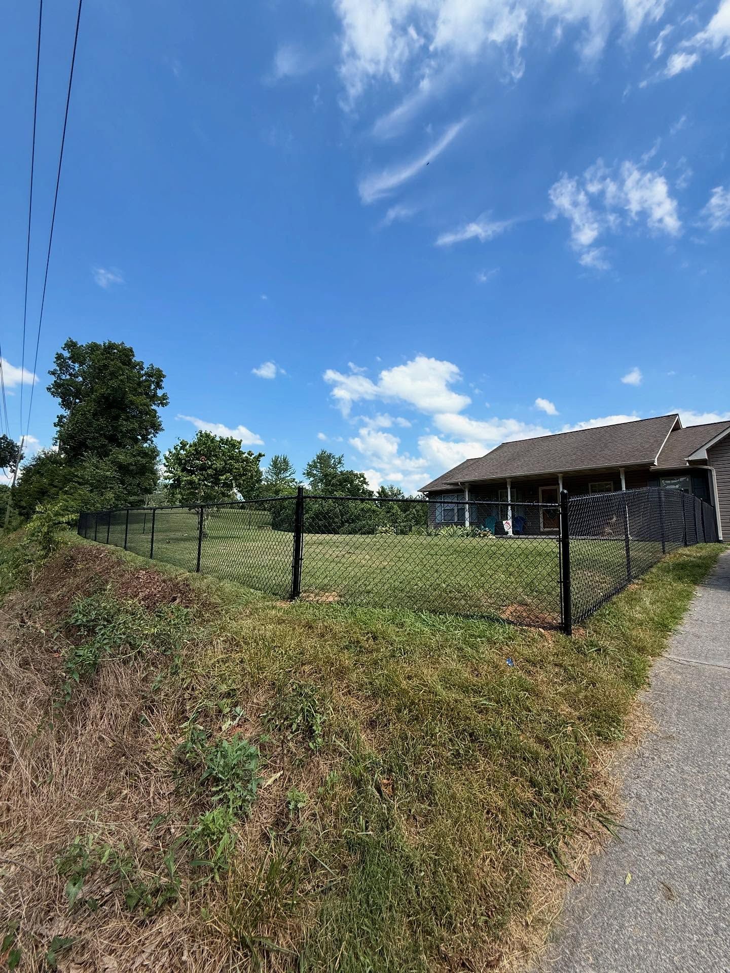 Rural house with a fenced grassy yard beside a road under a blue sky