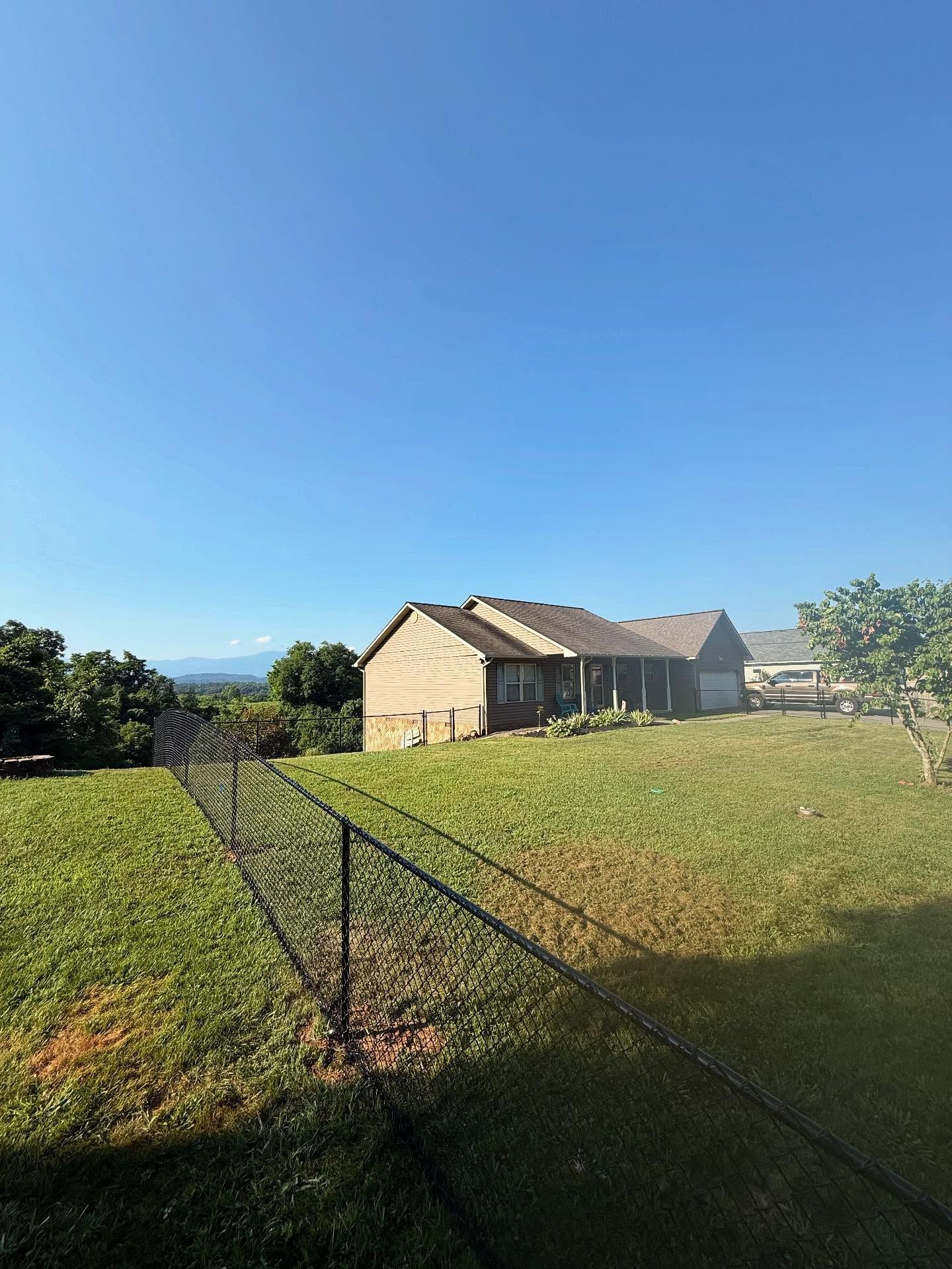 Fenced grassy field with a tan barn under a clear blue sky, viewed from a dirt path.