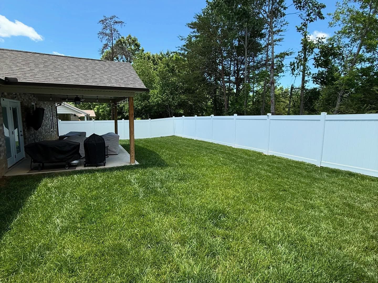 Backyard with green lawn, white fence, and covered patio under a blue sky