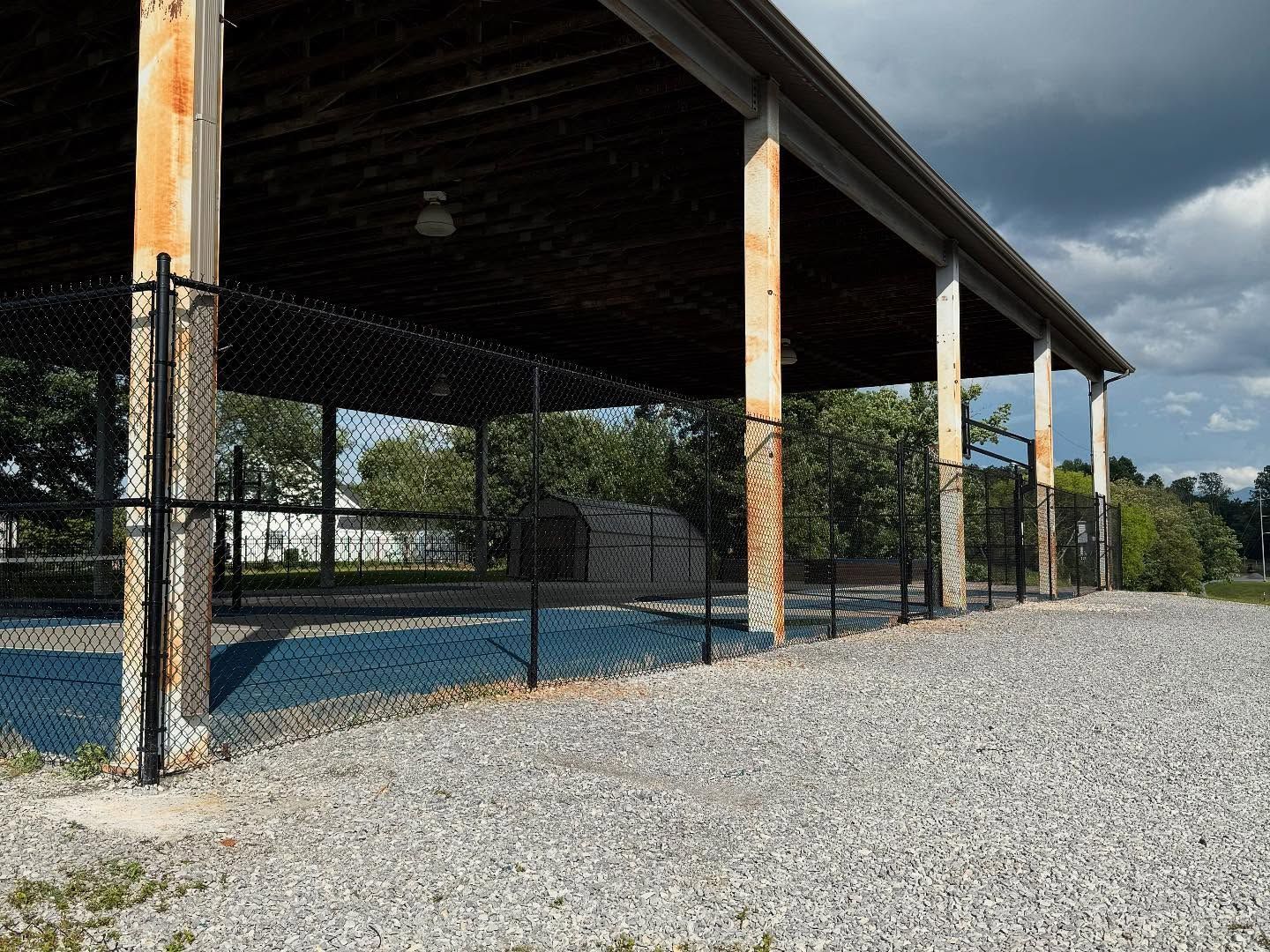 Open-air pavilion with chain-link fencing and gravel ground under a blue sky