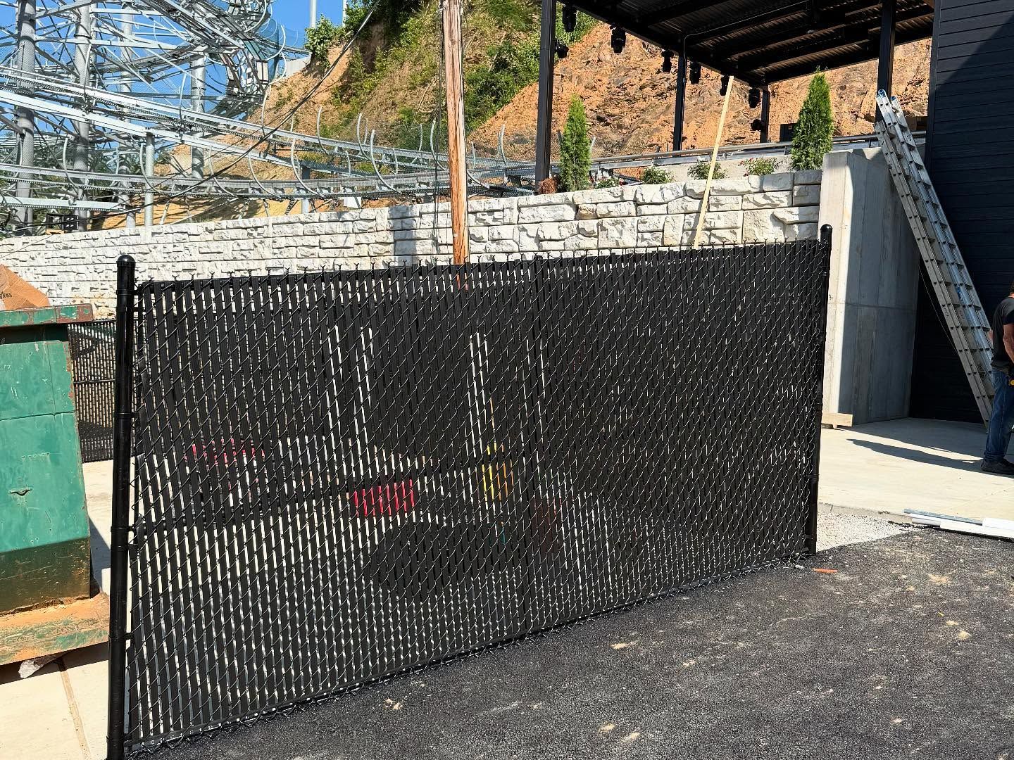 Black mesh safety fence around a construction area beside a concrete wall and metal structure.