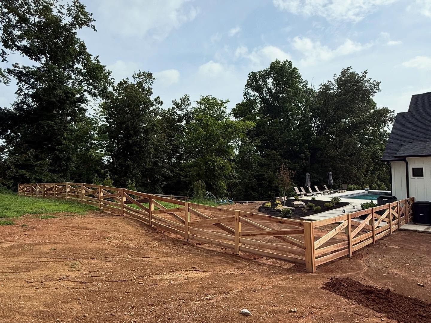 Wooded yard with a wooden fence and gate beside a house, with freshly cleared earth and mulch.