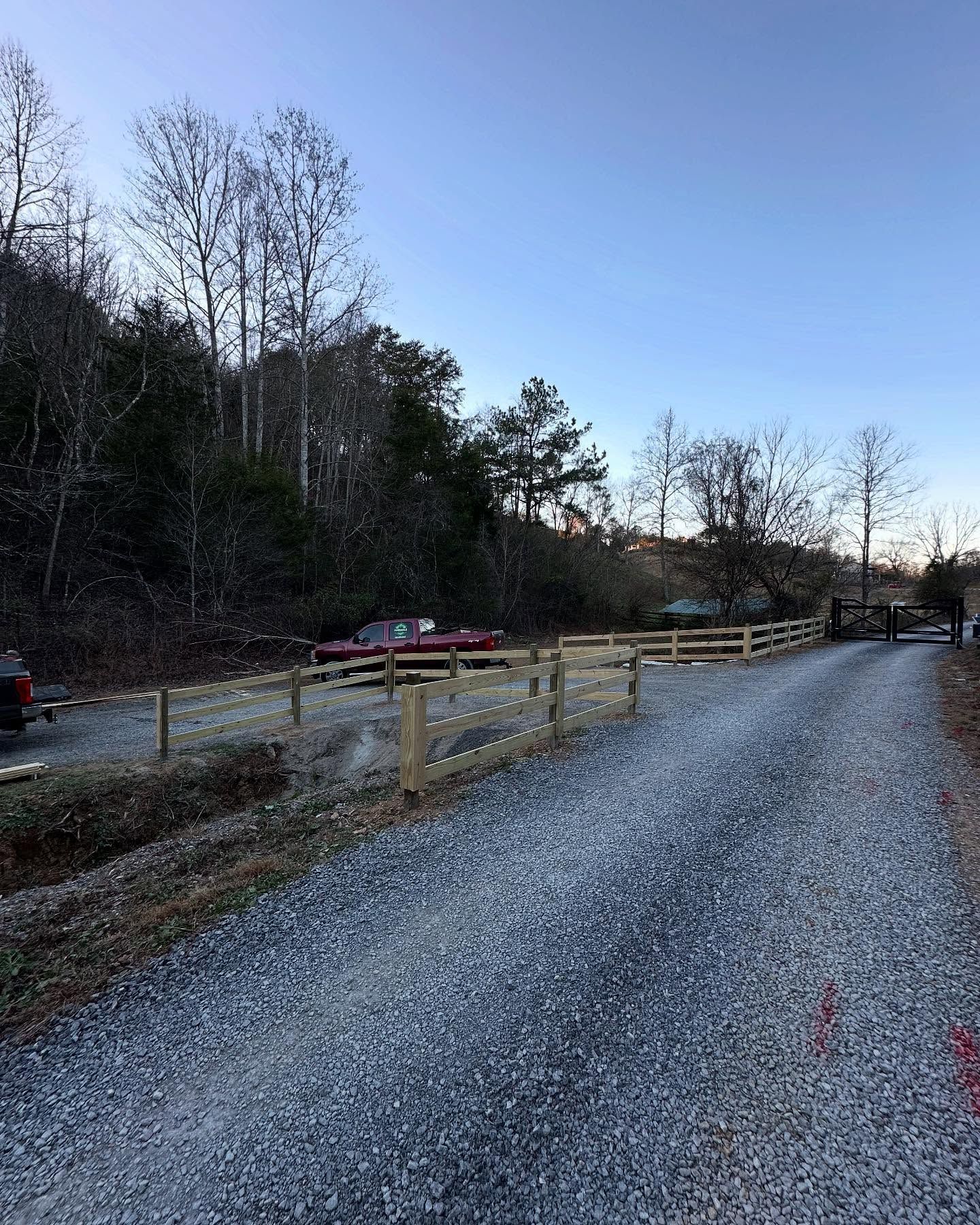 Gravel path beside a wooden fence and road, with bare trees under a clear blue sky at dusk