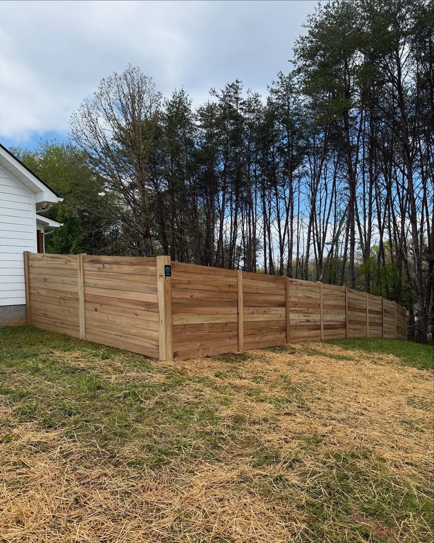 Wooden privacy fence along a grassy yard beside a house and trees