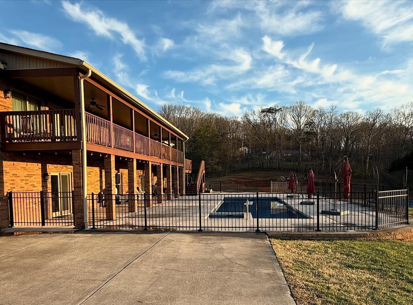 Outdoor pool beside a two-story brick building, with patio fencing and leafless trees under a blue sky