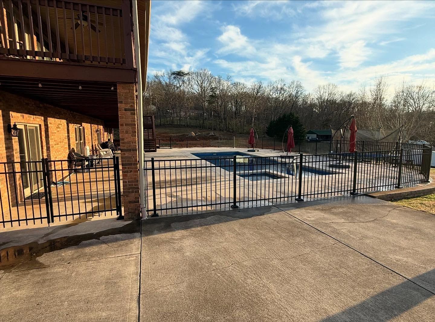 Outdoor pool with black fence beside a brick building, covered in snow under a clear sky.