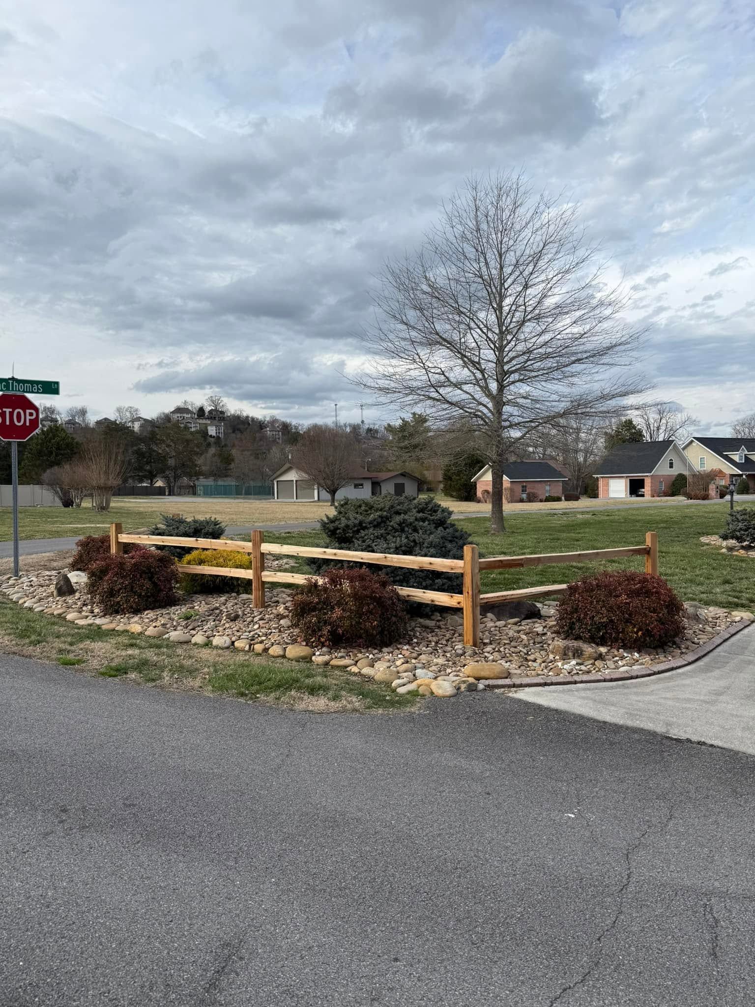 Landscaped neighborhood roundabout with stone border, mulch beds, a bare tree, and cloudy sky