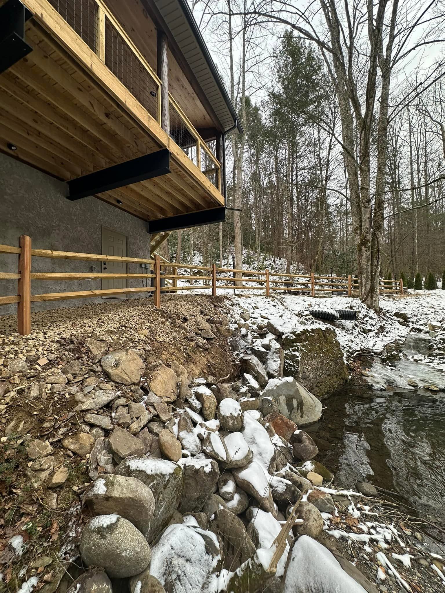 Wooden deck and retaining wall above a snowy rocky slope in a leafless forest