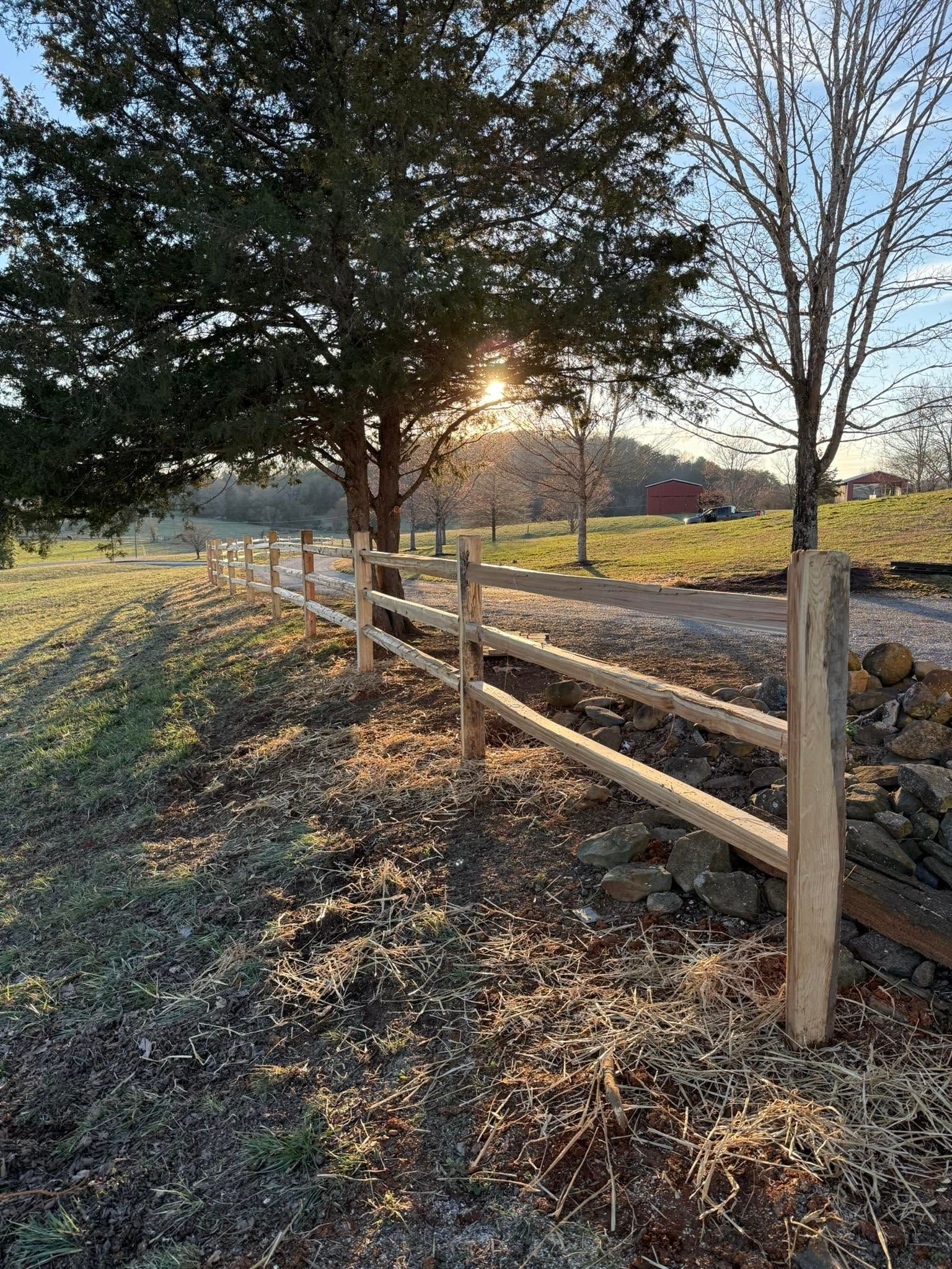 Sunlit wooden fence beside a frosty path with trees and fields at sunrise