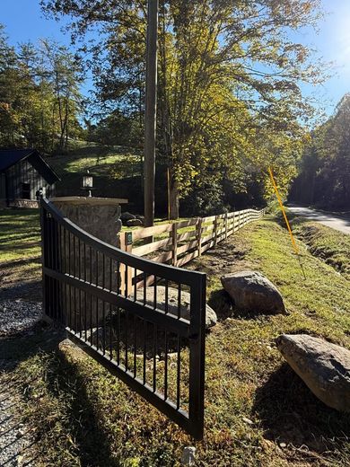 Open black metal gate beside a sunny gravel path with trees and rocks in a wooded yard