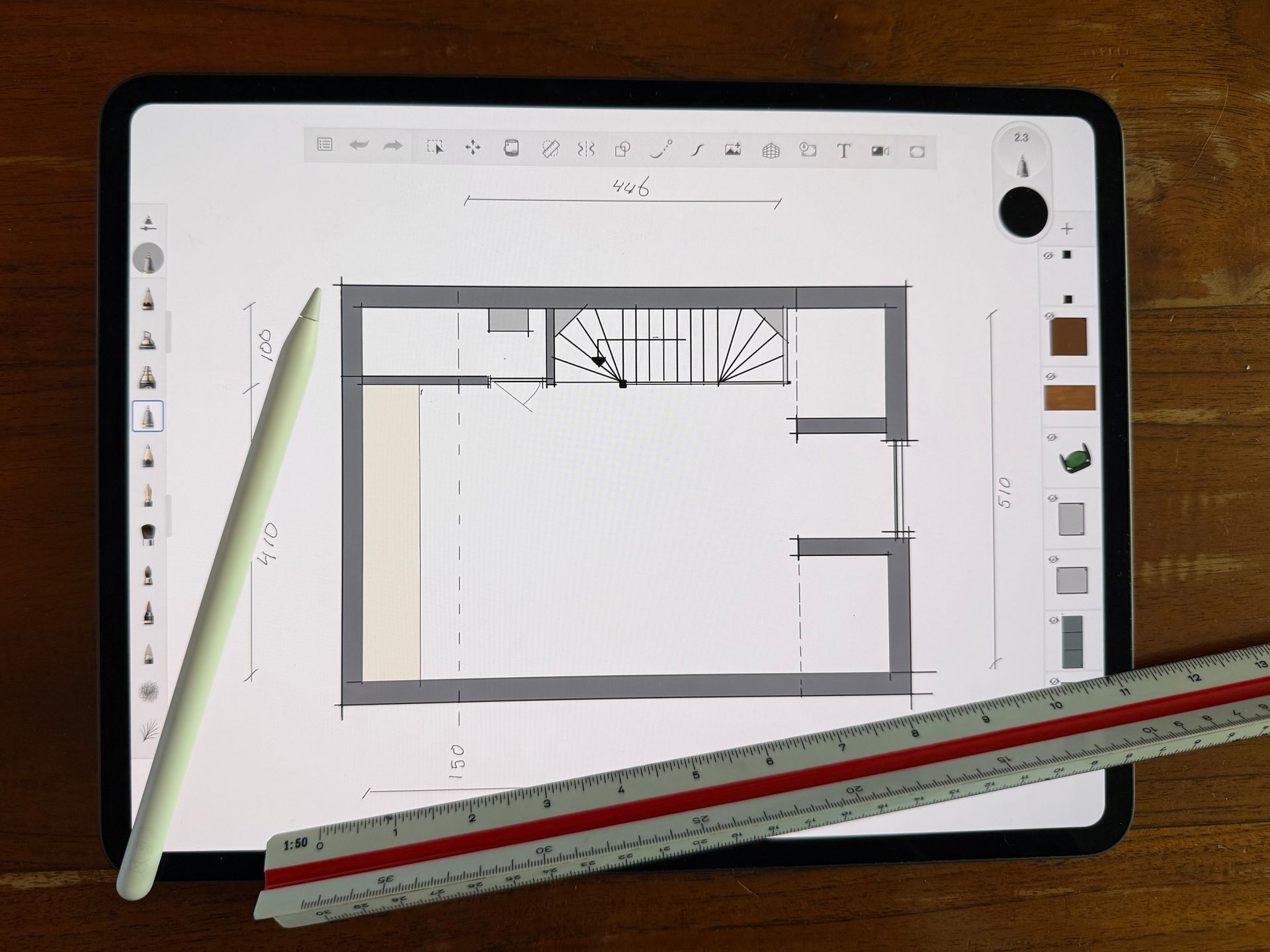 Tablet met een plattegrondschets, een witte stylus en een liniaal op een houten bureau.