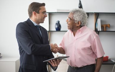 Two professionals shaking hands in an office while one holds a tablet