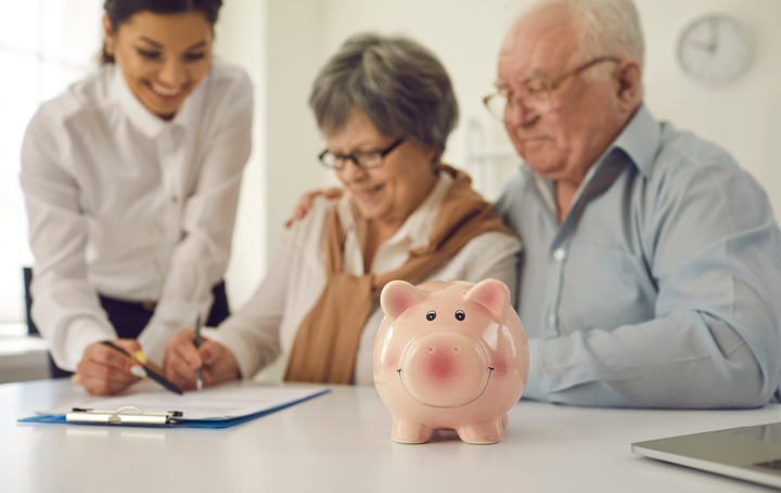 Three people reviewing documents with a pink piggy bank on a desk in an office