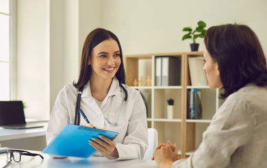 Doctor speaking with a patient in a bright office, holding a blue folder and smiling.