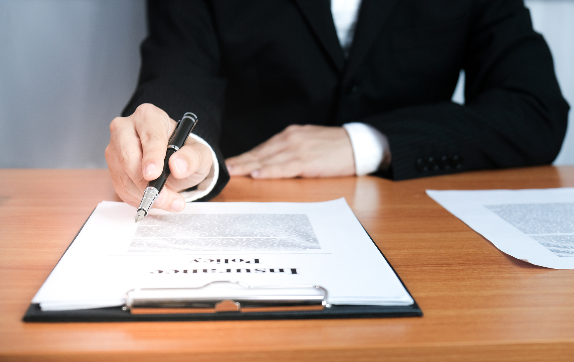 Person signing a document at a desk with a clipboard and pen