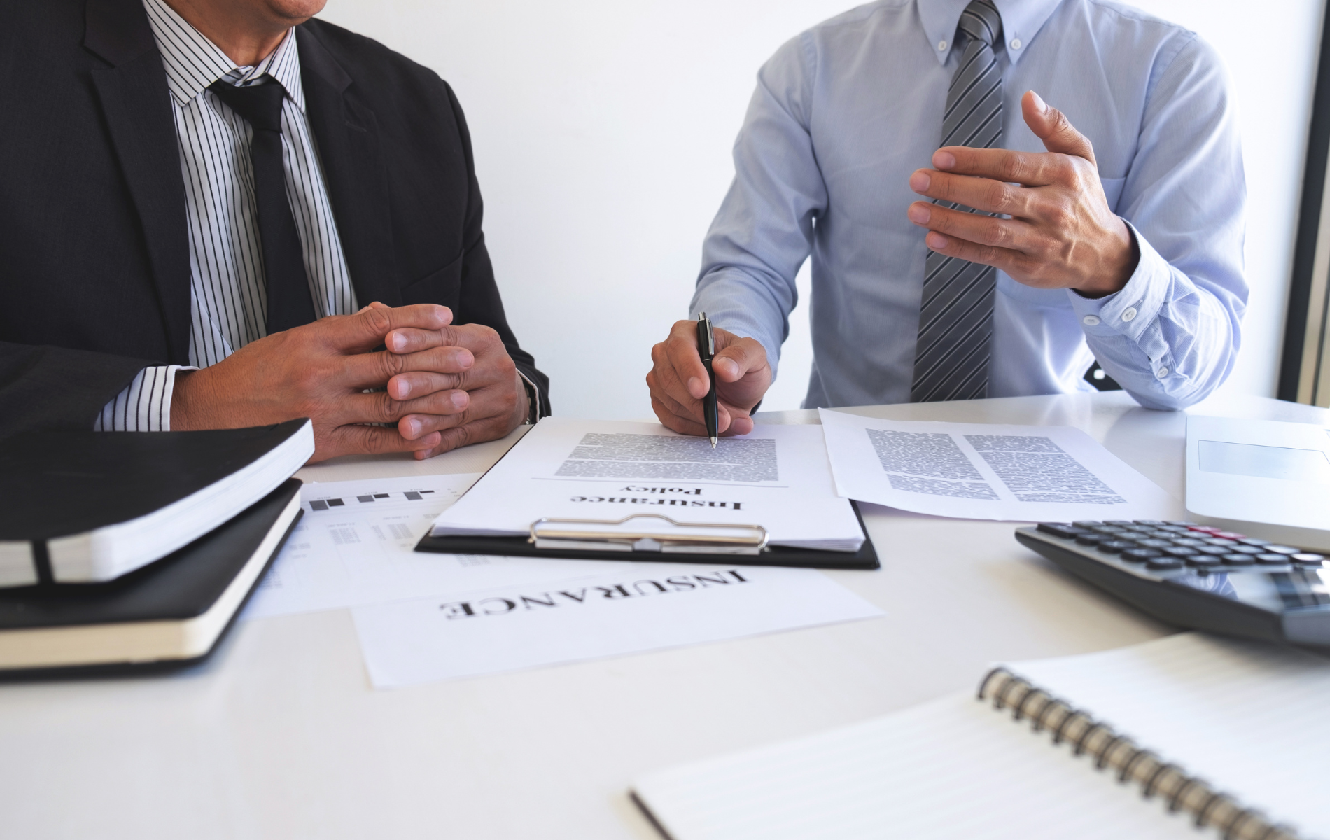 Two businesspeople in dress shirts discussing documents at a desk with a calculator and notebook