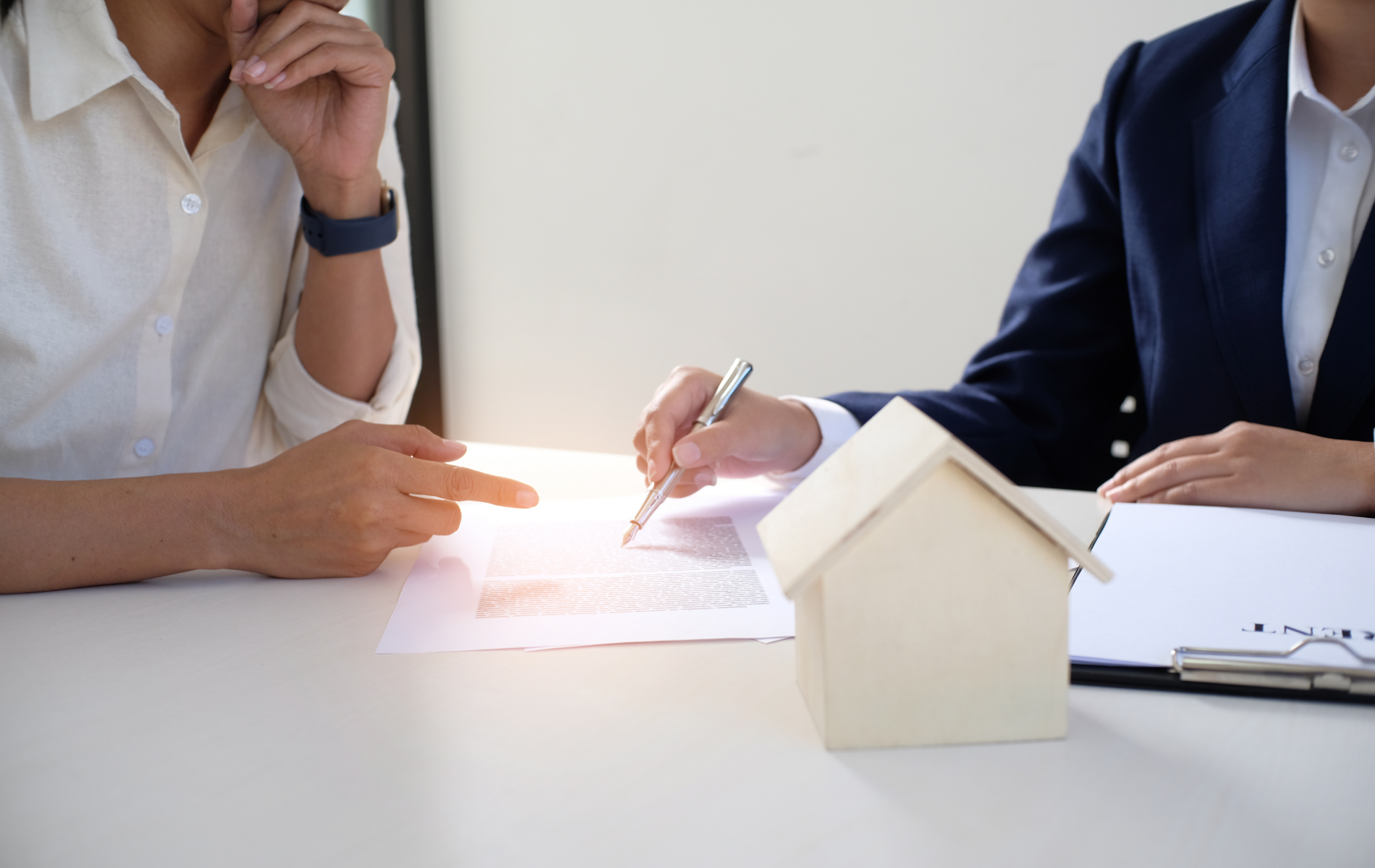 Two people reviewing mortgage documents beside a small house model at a desk