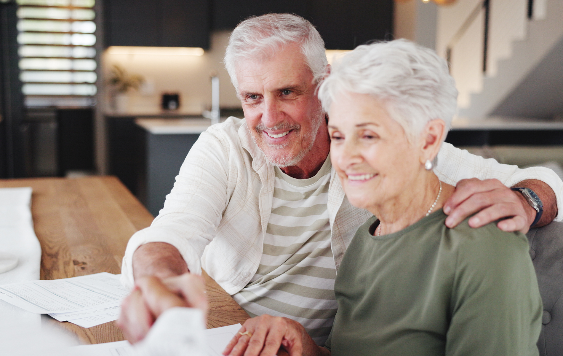 Smiling couple sitting at a table, looking at a document together in a cozy home setting