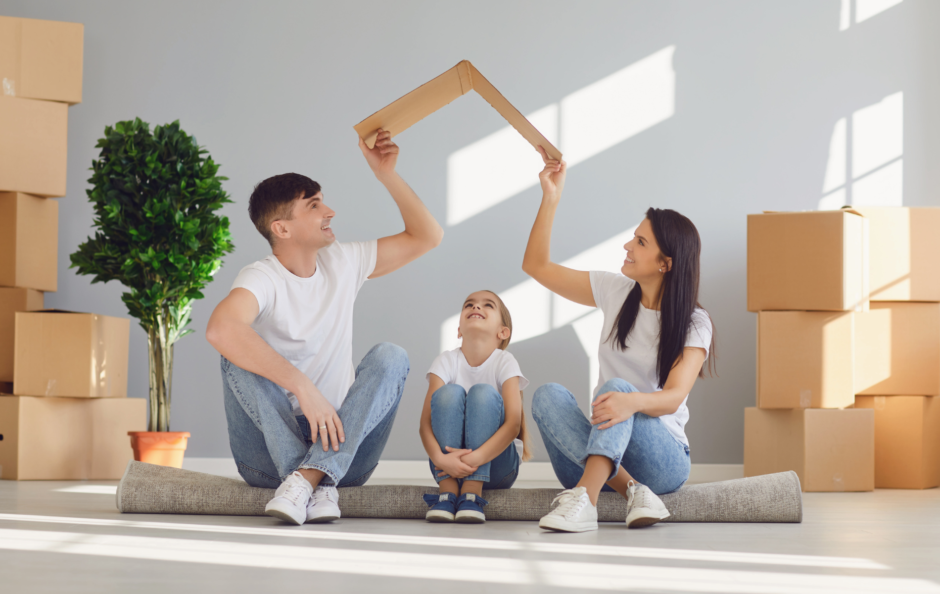 Family sitting on the floor opening a cardboard box in a bright, moving-day living room