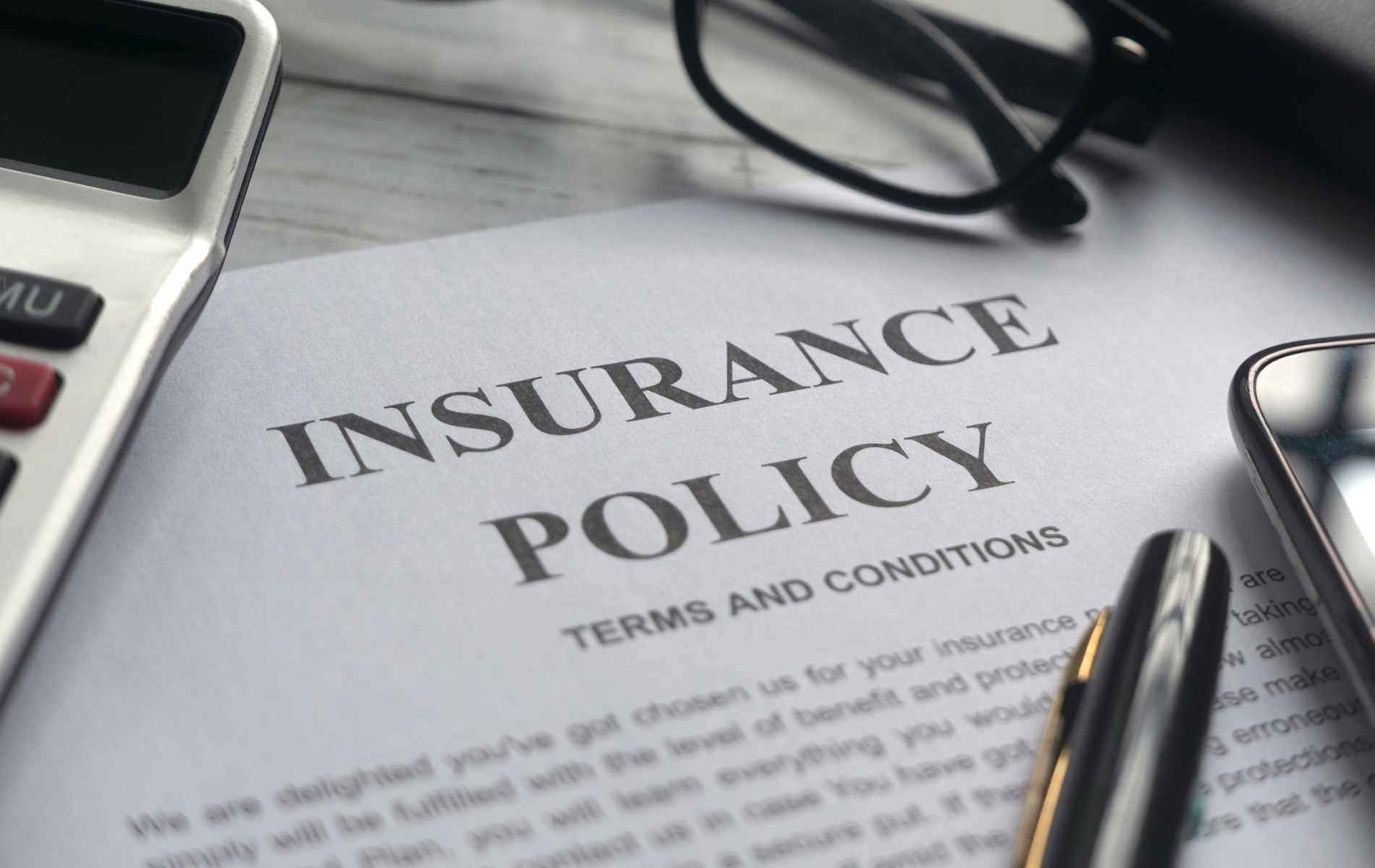 Insurance policy document with calculator, pen, and eyeglasses on a desk