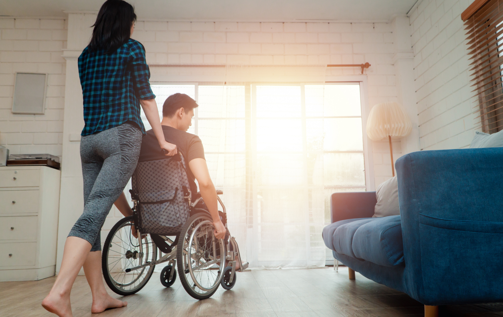 Person in wheelchair with a companion in a bright living room near a blue couch