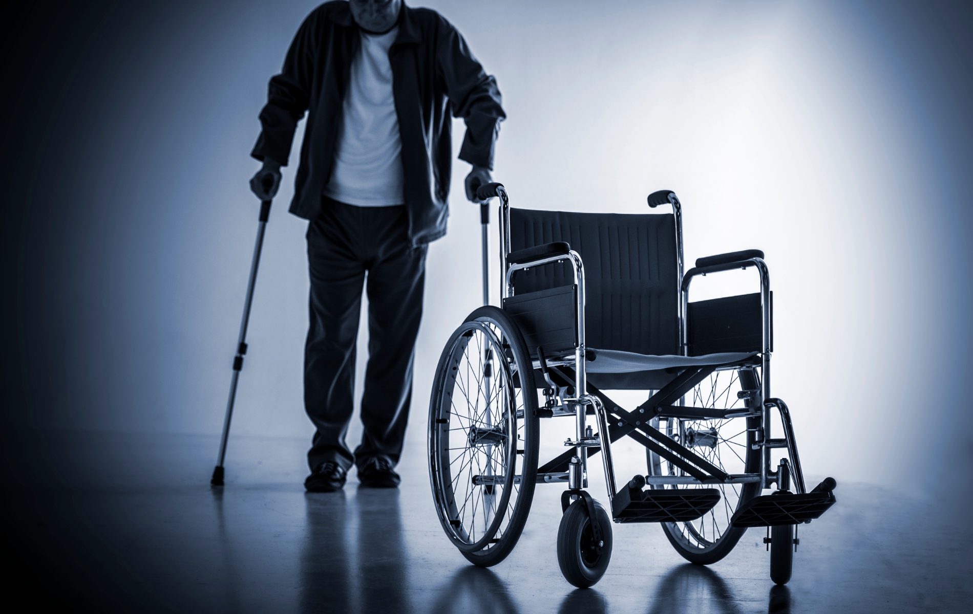 Person with crutch standing beside a wheelchair in a dimly lit room