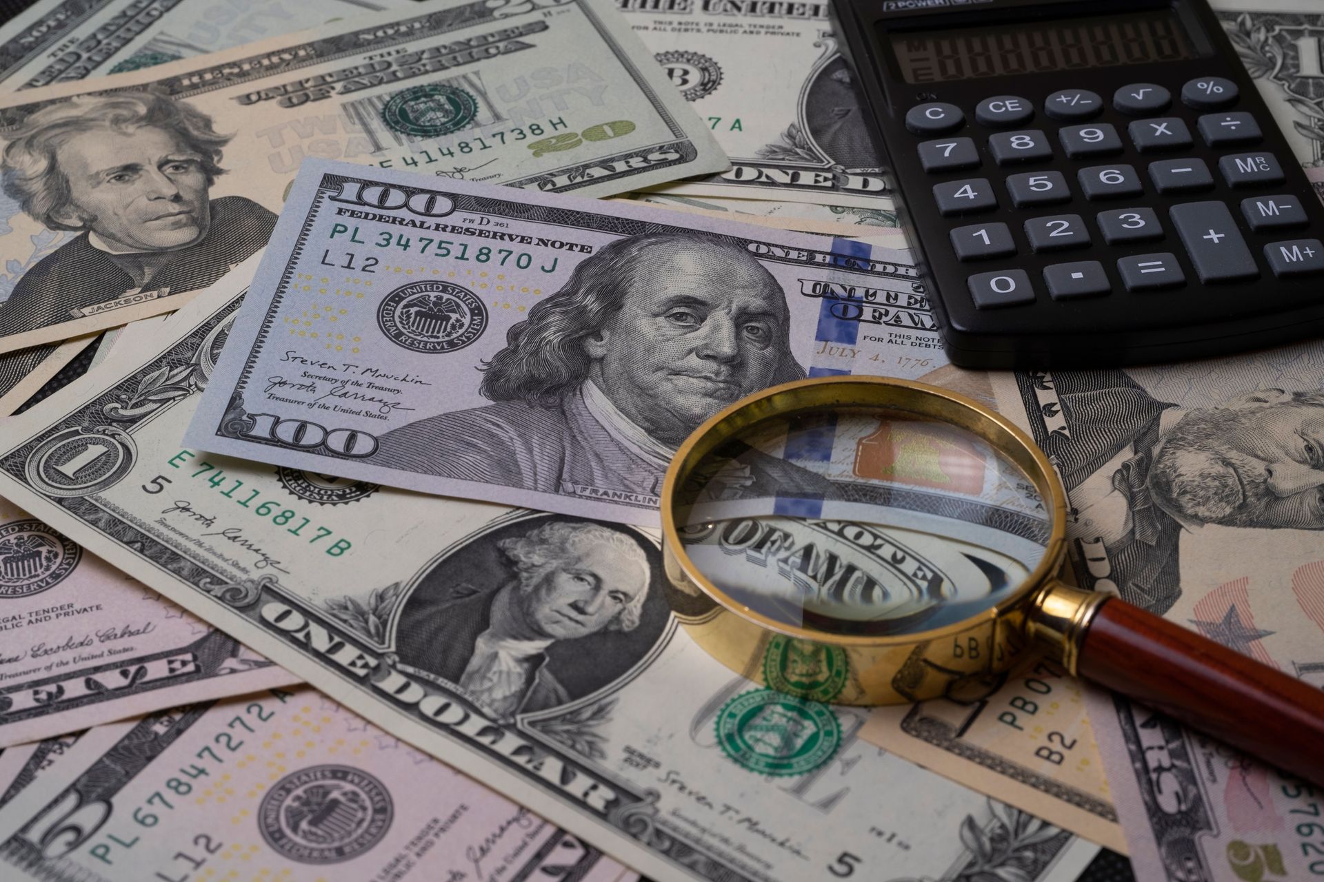 U.S. dollar bills with a calculator and magnifying glass on top